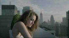 a beautiful young woman sitting on top of a roof next to a tall city skyline