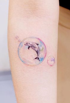 a woman's arm with a dolphin in a bubble tattoo on the left forearm