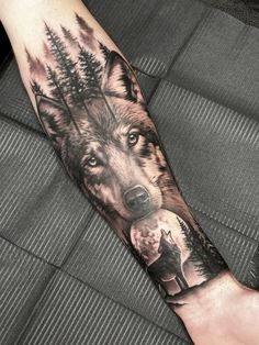 a man's arm with a wolf and pine trees tattoo on the left forearm