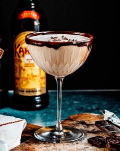 a close up of a drink in a coupe glass on a table with chocolate chunks