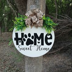 a sign that says home sweet home hanging on the side of a tree in front of some trees