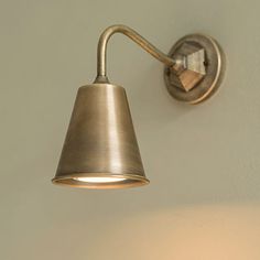 a wall light with a metal shade on it's side and a white wall in the background