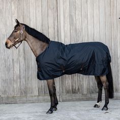 a horse wearing a blanket standing in front of a wooden fence with it's head turned to the side