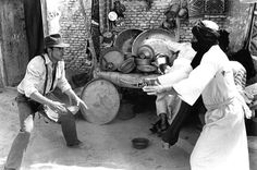 an old black and white photo of two people in front of a stove with pots on it