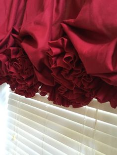 red ruffled curtains hanging on the side of a window sill with white blinds