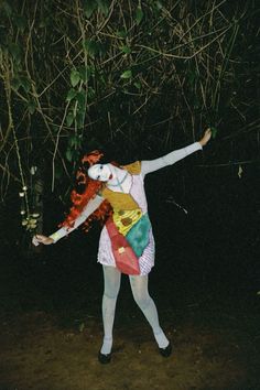 a woman dressed as a clown standing in the dark with her arms outstretched and legs spread out