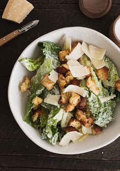 a white bowl filled with lettuce and croutons on top of a wooden table