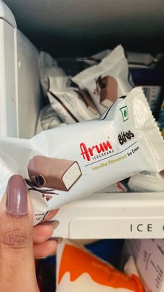 a hand holding a tube of toothpaste in front of an open refrigerator door