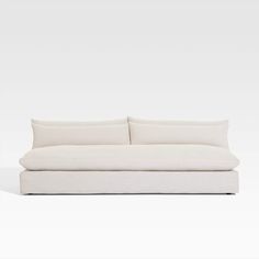 a white couch sitting on top of a white floor next to a wall with two pillows