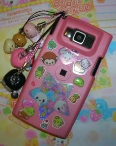 a pink cell phone with various stickers on it and a keychain attached to it