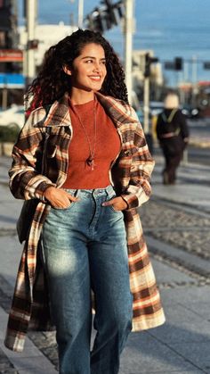 a woman is walking down the street with her hands in her pockets and wearing jeans