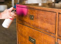 a person spray painting a wooden dresser with pink and white paint on the drawer top