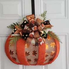 a decorative pumpkin hanging on the front door with fall leaves and ribbons attached to it