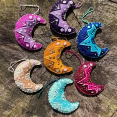 six different colored leather moon ornaments sitting on top of a piece of wood