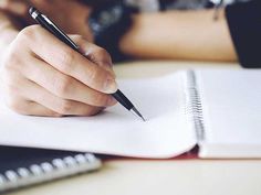 a person writing on a notebook with a pen in their left hand and a notepad next to them