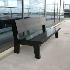 a wooden bench sitting in front of a glass window on top of a building next to a sidewalk