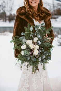 a woman in a fur coat holding a bouquet with white flowers and greenery on it