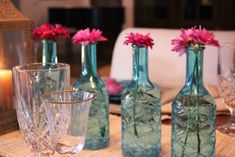 several vases with flowers in them sitting on a table next to glasses and candles