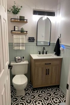 a white toilet sitting next to a sink in a bathroom under a mirror above a wooden cabinet