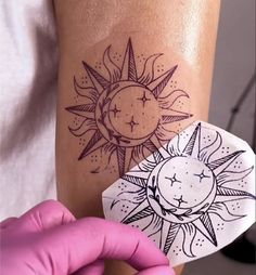 a person holding up a piece of paper with a sun and moon tattoo on it