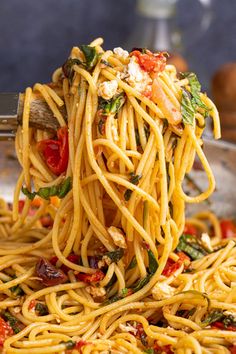 a fork full of pasta with spinach and tomatoes