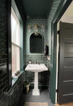 a bathroom with green and black tiles on the walls, white pedestal sink and mirror