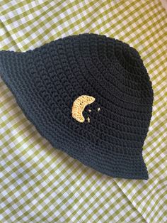 a black crocheted hat with a gold crescent on the side sitting on a green and white checkered table cloth