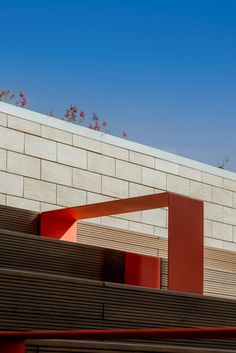 a red sculpture is in front of a brick wall with flowers growing on the top