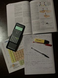 a calculator sitting on top of an open book next to some pens and markers