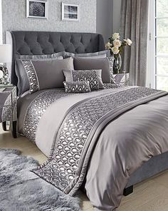 a bed with grey and white comforters in a bedroom next to a window,