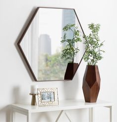 a white table with two vases and a mirror on it next to a plant