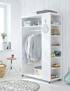 an open white closet with clothes hanging on the rack and other items in front of it