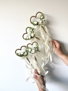 someone is holding some flowers in the shape of hearts on a white wall with ribbons attached to it