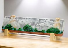 a wooden table topped with a glass vase filled with green trees and rocks on top of it