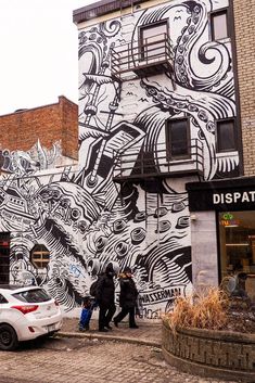 two people standing in front of a building with a mural on it's side