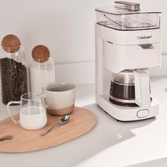 a white coffee maker sitting on top of a counter next to a cup and spoon