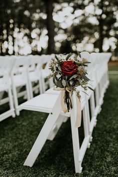 a bouquet of flowers sitting on top of a wooden bench next to white folding chairs