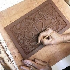 a man is working on a carving in the shape of a square with letters and numbers