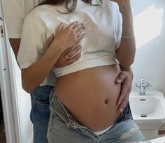 a pregnant woman is taking a selfie in the mirror with her cell phone and looking at her stomach