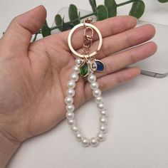 a hand holding a keychain with pearls and charms