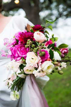 a bride holding a bouquet of pink and white flowers on her wedding day in the park