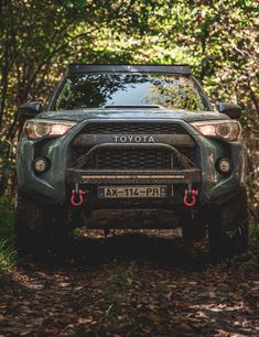 the front end of a green toyota truck parked on a dirt road surrounded by trees