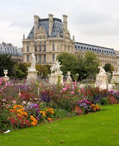 a garden with many flowers and statues in front of a large building