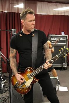 a man in black shirt playing an electric guitar with other instruments behind him on stage