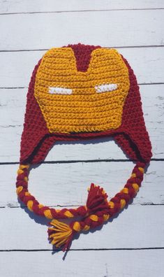 a crocheted iron man hat on top of a white wooden table with a red and yellow tassel