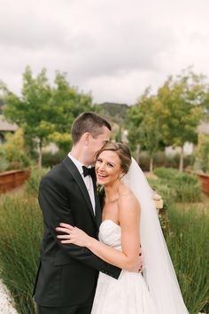 a bride and groom standing together in front of some tall grass