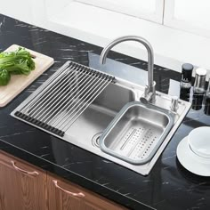 a stainless steel kitchen sink with drainer, strainer and cutting board on the counter