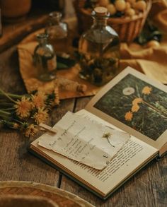 an open book sitting on top of a wooden table next to some flowers and jars