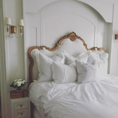 a white bed topped with lots of pillows next to a night stand and two nightstands