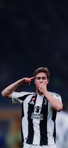 a young man standing on top of a soccer field holding his finger to his mouth